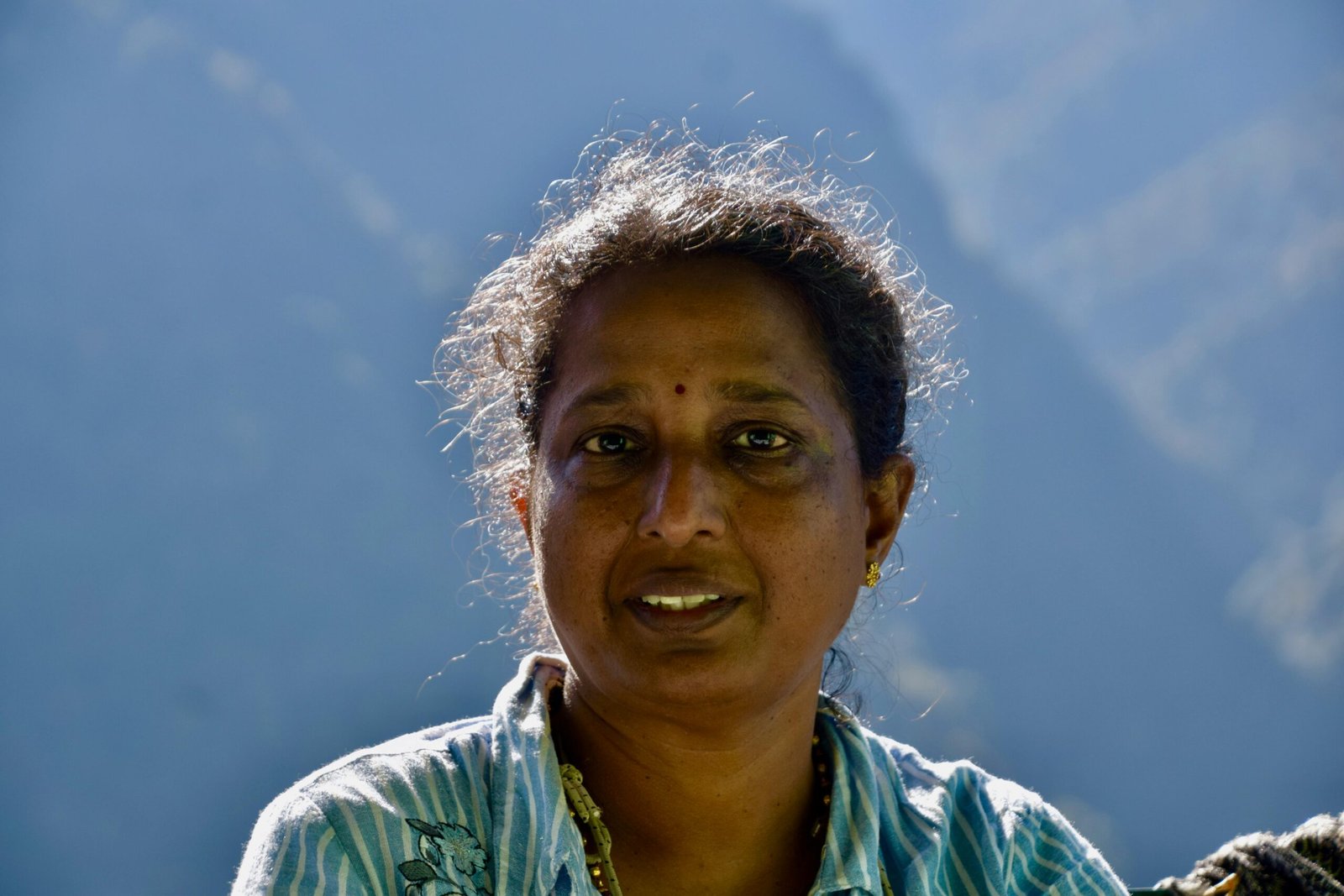 Close-up portrait of a woman in natural light with mountainous backdrop.